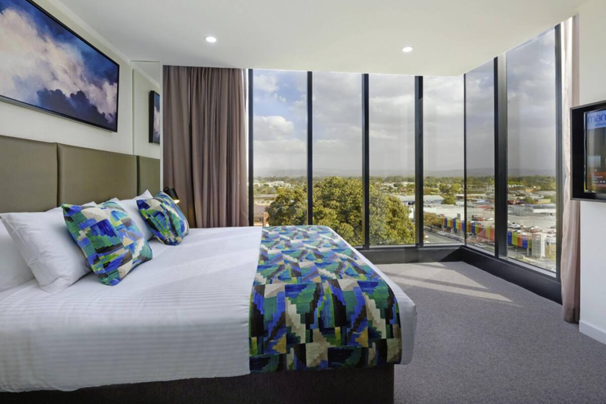 Une chambre d’hôtel avec un grand lit, une vue sur la ville et un téléviseur fixé au mur.