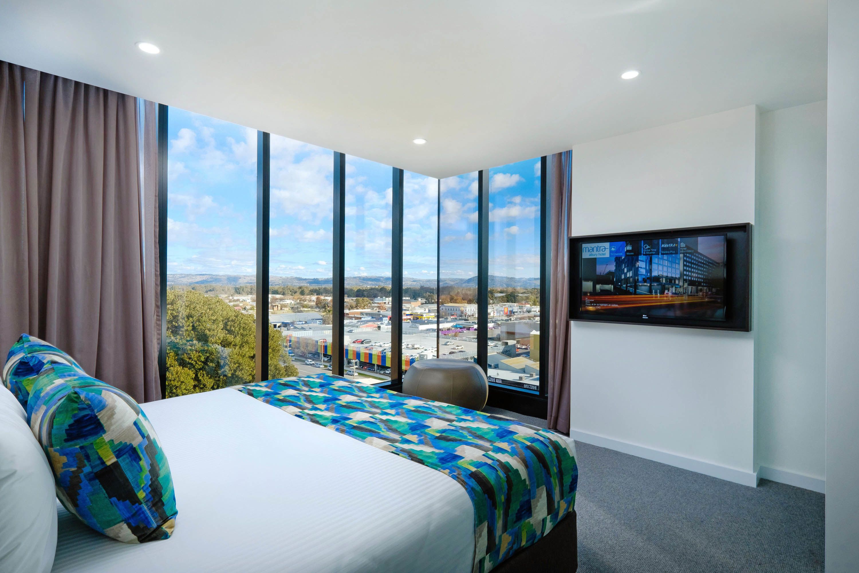 Ein Hotelzimmer mit einem großen Bett, Blick auf eine Stadtkulisse durch raumhohe Fenster, einem flachbildfernseher an der Wand und einem kleinen Fitnessball.
