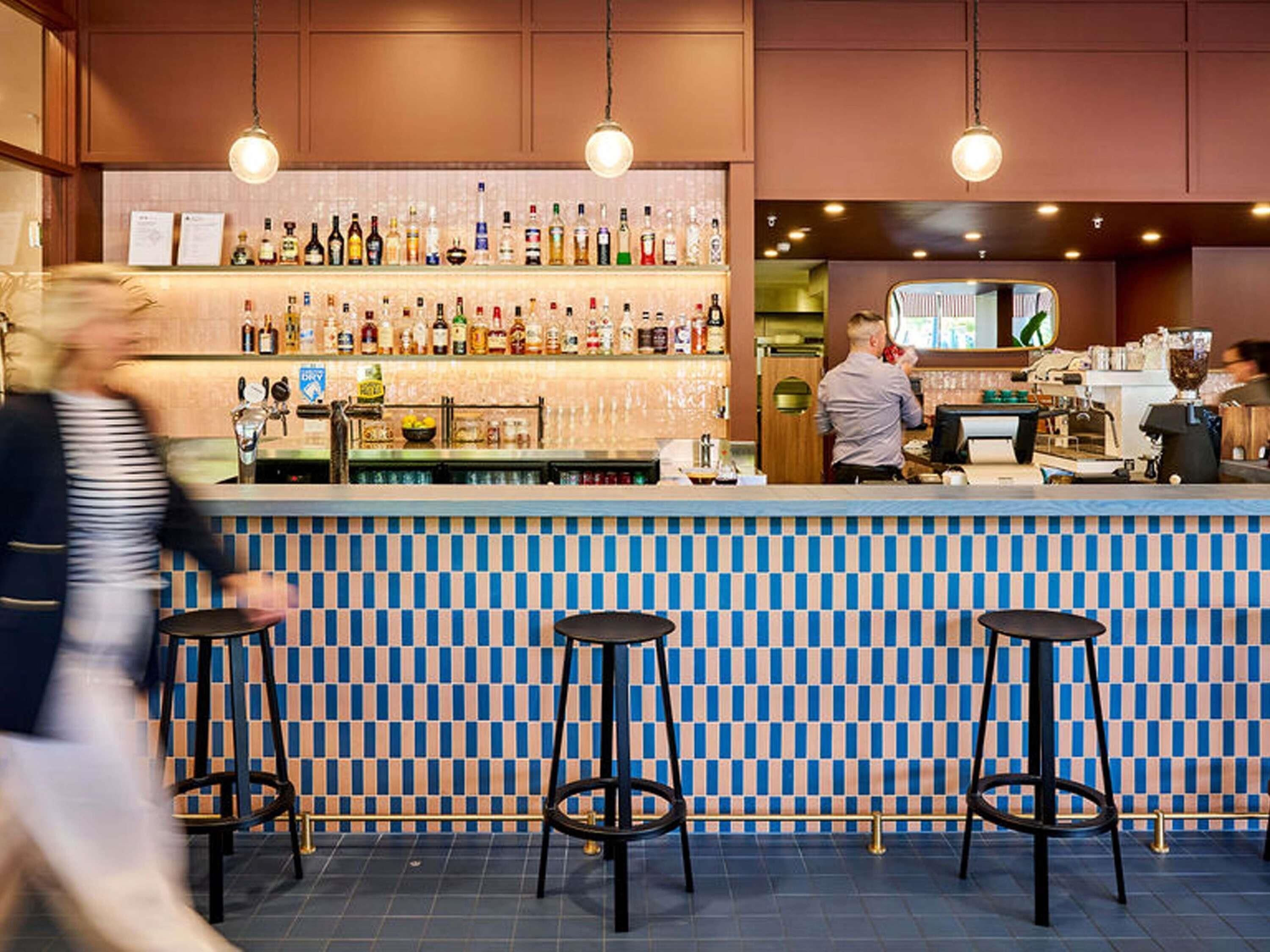 A bar area with a checkered tile backsplash, bar stools, and a variety of bottles on shelves.