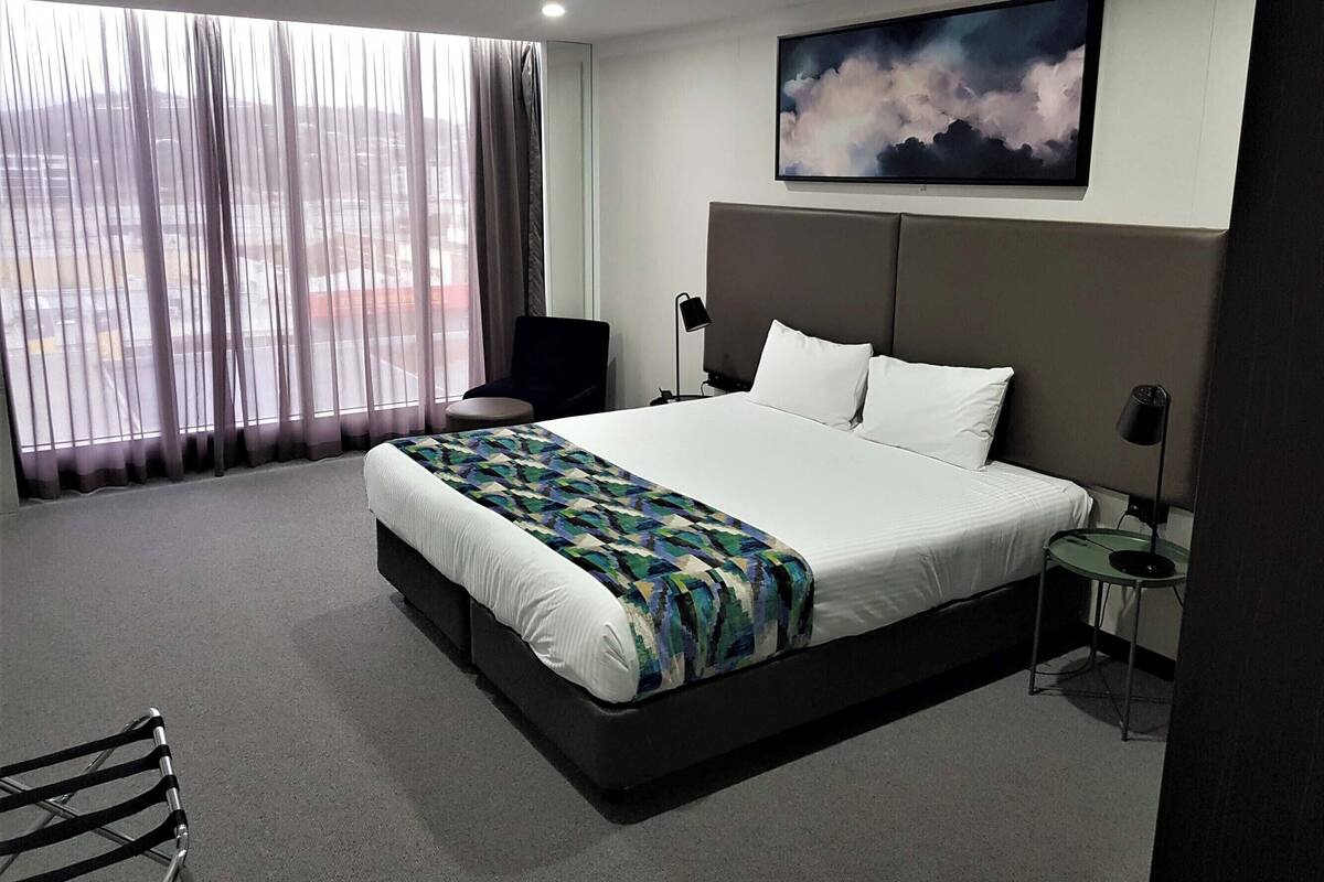 Une chambre d’hôtel moderne avec un grand lit, une chaise, un bureau et un tableau au mur.