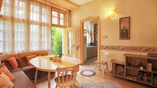 Uma sala de estar aconchegante com um sofá, uma mesa de jantar e cadeiras. Uma cozinha fica visível por uma porta aberta.