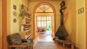 Uma sala de estar acolhedora com lareira, soalho de madeira e uma área de jantar visível através de um arco.