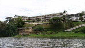 Un immeuble à plusieurs étages doté de balcons, situé près d’une étendue d’eau et entouré de verdure.