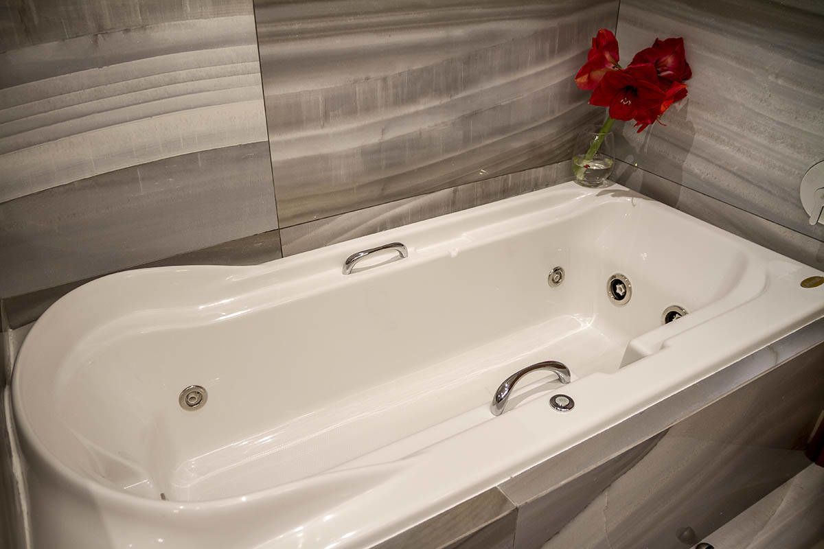 A modern bathroom with a large bathtub, a handheld showerhead, and a small vase with red flowers.