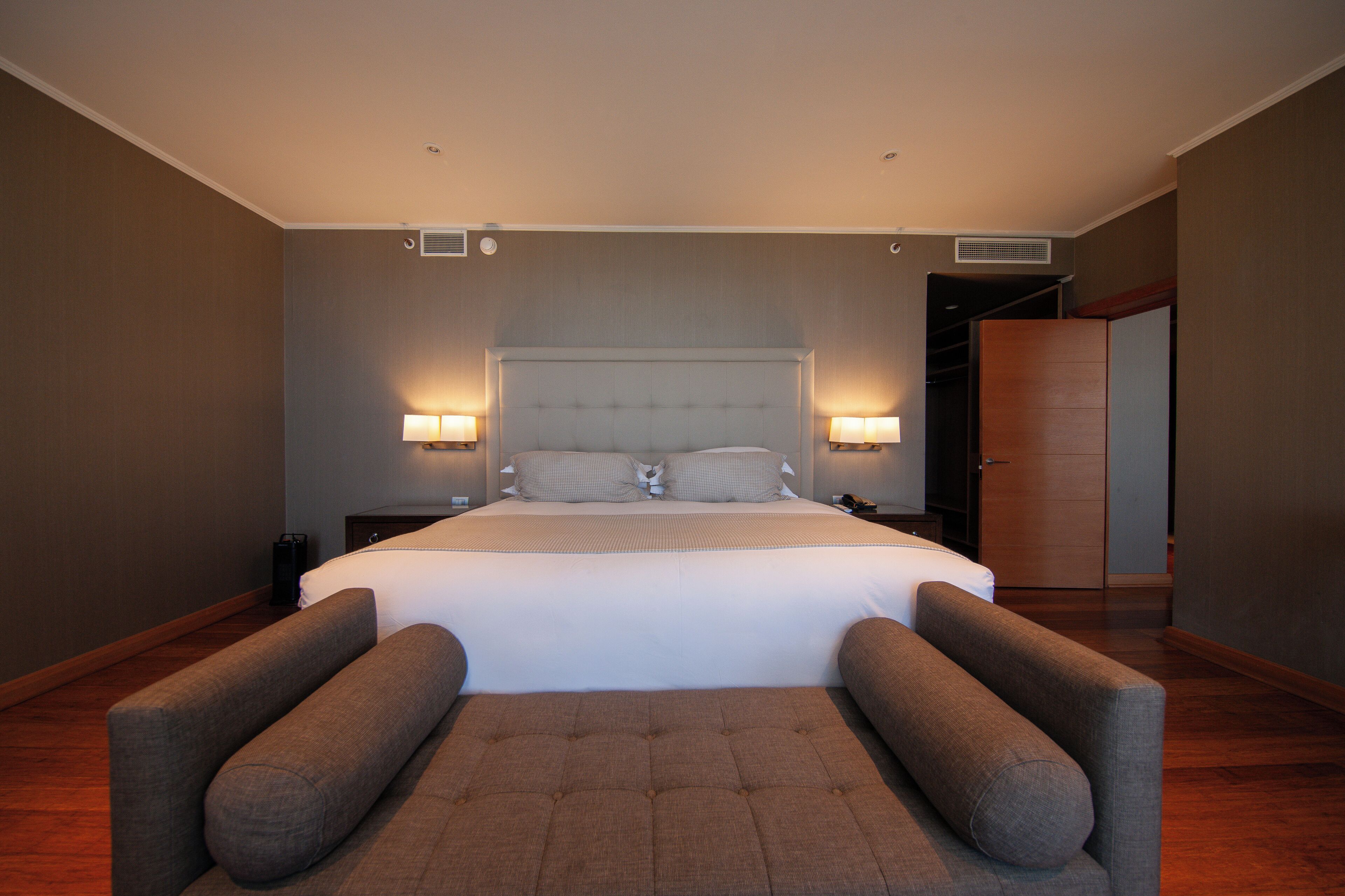 Habitación de hotel con una cama grande, dos mesitas de noche, un armario y una zona de estar con dos sillones.