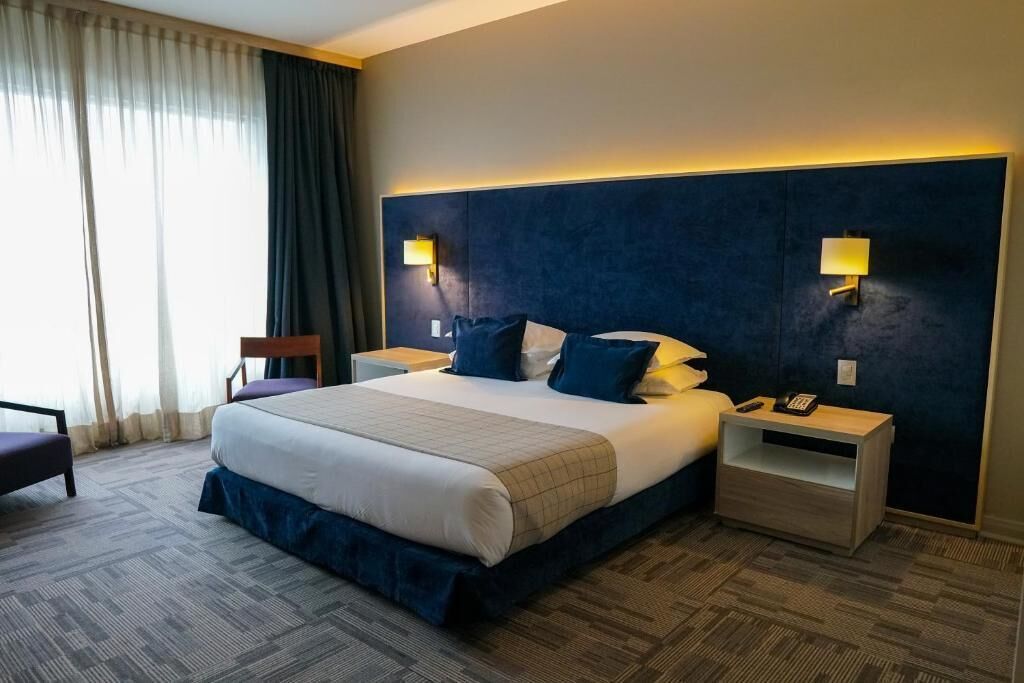 Une chambre d’hôtel avec un grand lit, deux tables de chevet, une chaise et une vue sur le paysage urbain par la fenêtre.