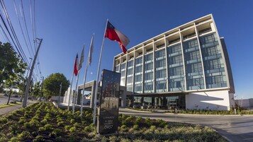 Un moderno edificio de hotel con fachada de vidrio, varias banderas y un jardín paisajista.