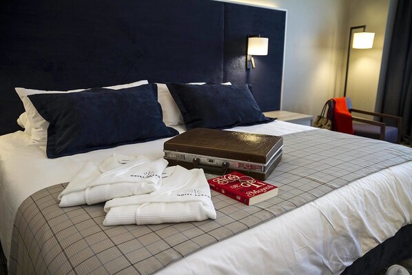 A neatly made bed with a checkered bedspread, two pillows, a book, and folded towels. - Hotel Parada Linares (Linares)