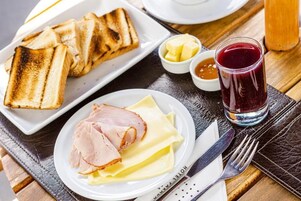 Un plato de desayuno con tostadas, jamón y queso, acompañado de mantequilla y mermelada.
