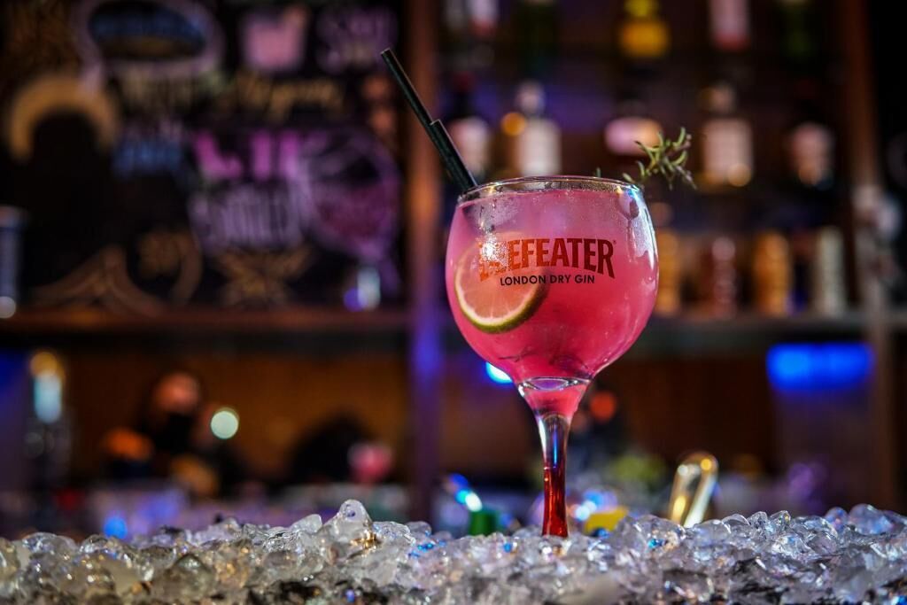 A cocktail glass labeled "Efeater London Dry Gin" on a bar counter with ice.