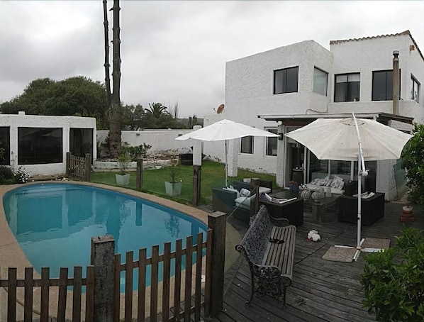 A poolside area with a wooden deck, outdoor furniture, and umbrellas. - Casa Av. Costanera sn Sector Casino (Coquimbo)