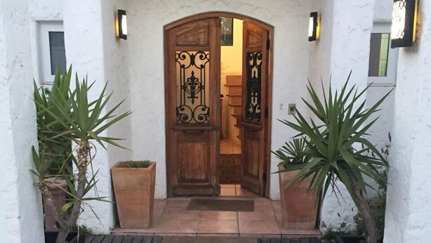 A wooden door with intricate metalwork, flanked by potted plants, leading to a tiled entrance area. - Casa Av. Costanera sn Sector Casino (Coquimbo)