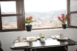 Una mesa con vistas a una ciudad a través de una ventana, dos plantas en macetas y algunas tazas y platos.