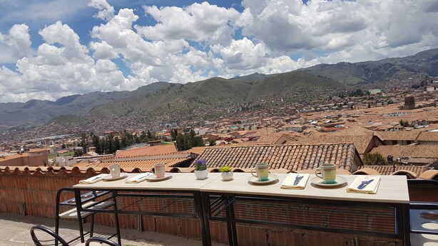 A table set outdoors with chairs, overlooking a cityscape and mountains. - Marco Wasi - San Blas (Cusco)