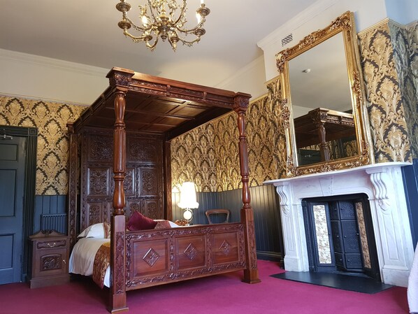 A four-poster bed with intricate carvings, a large ornate mirror, and a fireplace. - The Gothic Mansion (Bristol)