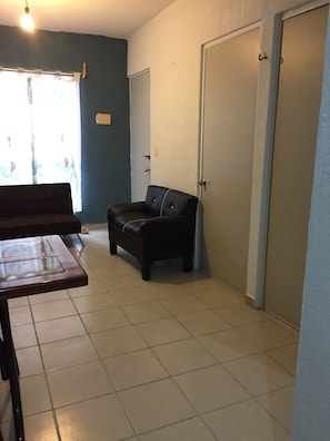 A room with a sofa, a small black chair, a table, and a door. - Apartamento PlayaDelCarmen 627 by Sinbad (Playa del Carmen)