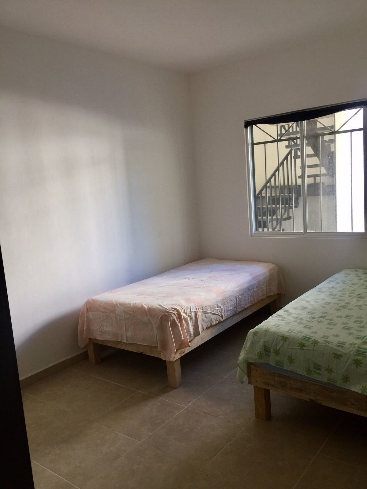 A small, sparsely furnished room with two single beds, a window with a view of a staircase, and tiled flooring.