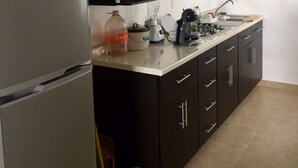 Eine moderne Küche mit dunklen Schränken, einem Edelstahlkühlschrank, einer Arbeitsplatte mit verschiedenen Geräten und einem Fliesenboden.