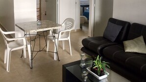 Ein Wohnzimmer mit einem Esstisch, weißen Stühlen, einem schwarzen Ledersofa und einem Couchtisch mit einer Pflanze.
