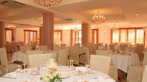 Una sala da banchetti con tavoli rotondi apparecchiati per la cena, ognuno con tovaglie bianche, bicchieri e piatti di cibo.