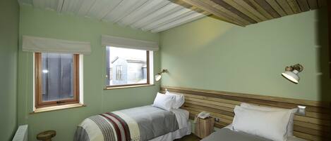 Un dormitorio con dos camas, techo de madera y dos ventanas con persianas blancas.