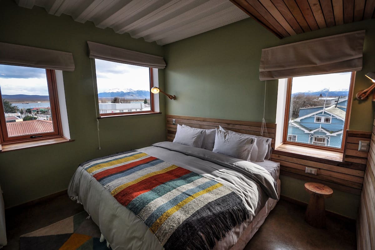 A bedroom with a bed, a window with a view of mountains, and a small wooden table.