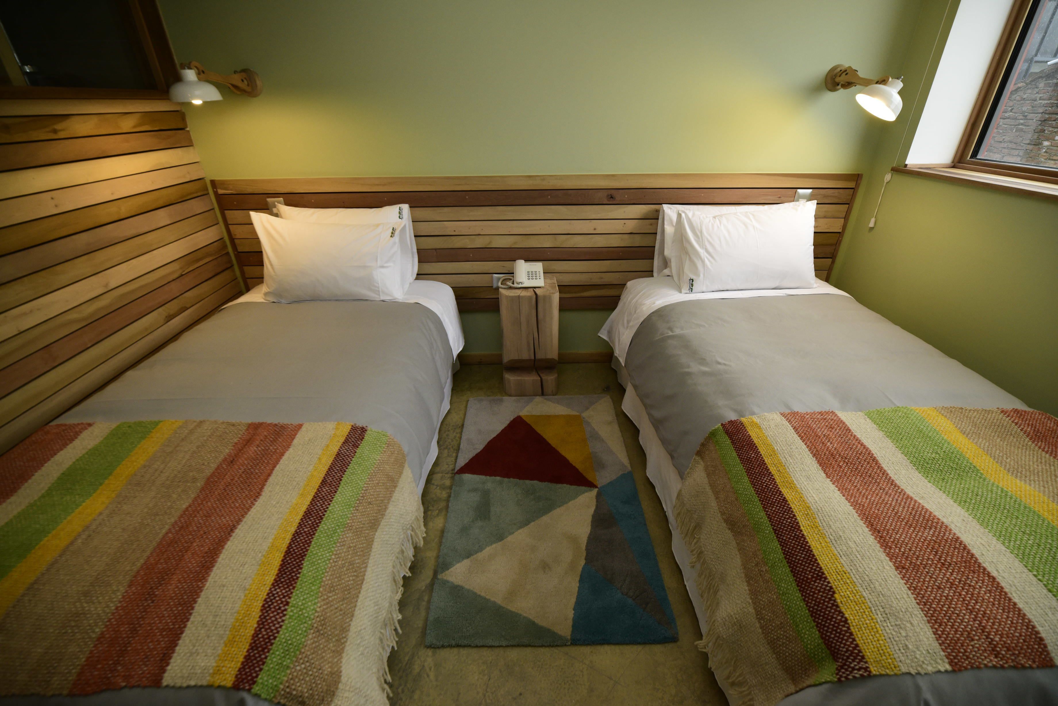 A room with two beds, a wooden headboard, a small table with a phone, and a window.