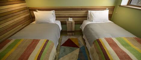 A room with two beds, a wooden headboard, a small table with a phone, and a window.