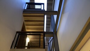 Un intérieur à plusieurs niveaux, agrémenté d’un escalier en bois, d’un luminaire suspendu et d’un élément décoratif fixé au mur.