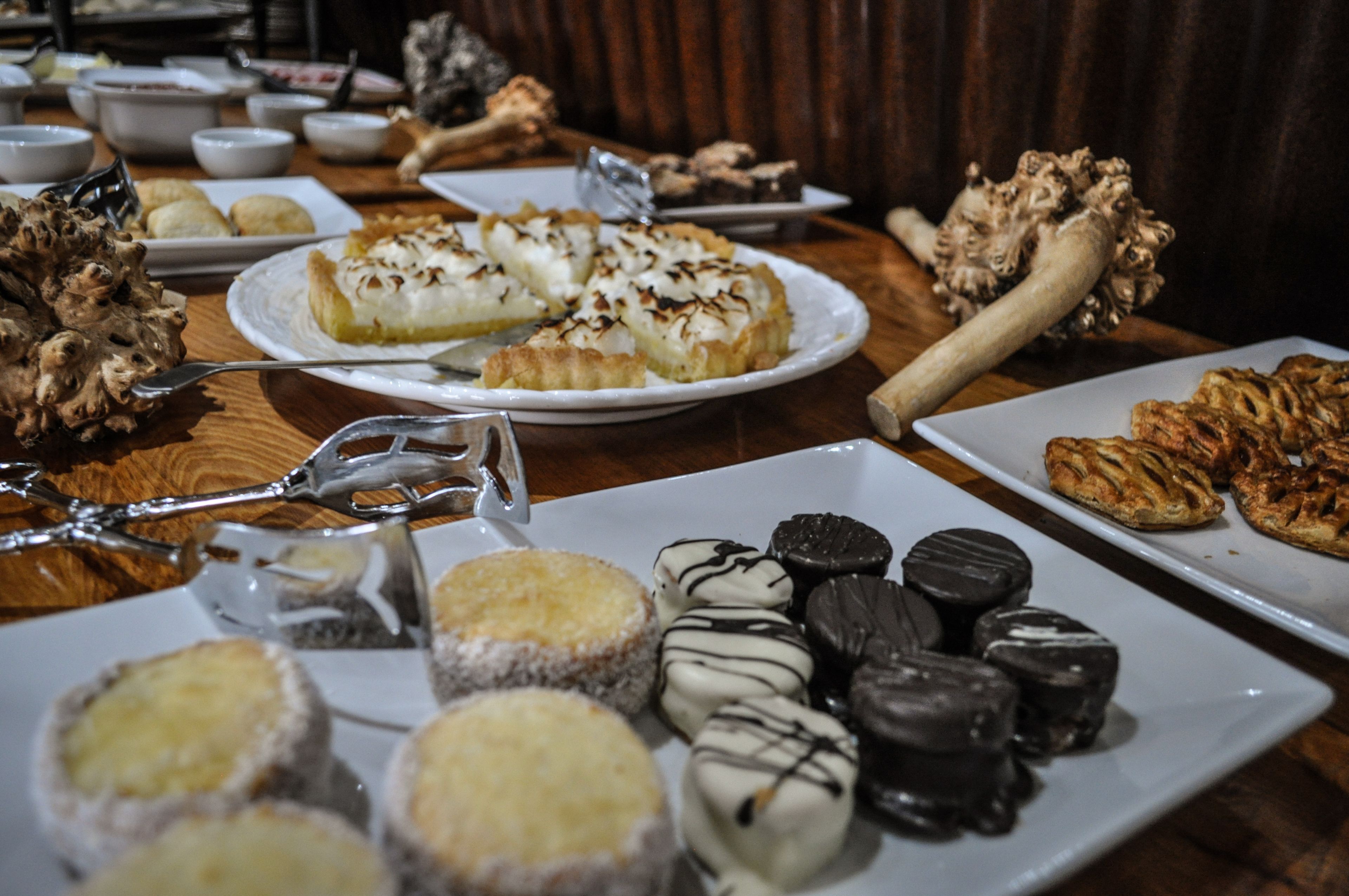 Uma mesa com diversos doces e pâtisseries, incluindo uma torta com crosta dourada e um prato de guloseimas cobertas de chocolate.