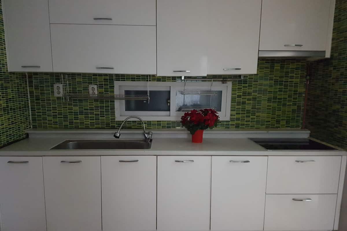 A modern kitchen with white cabinets, a stainless steel sink, a microwave, and a red flower vase on the countertop.