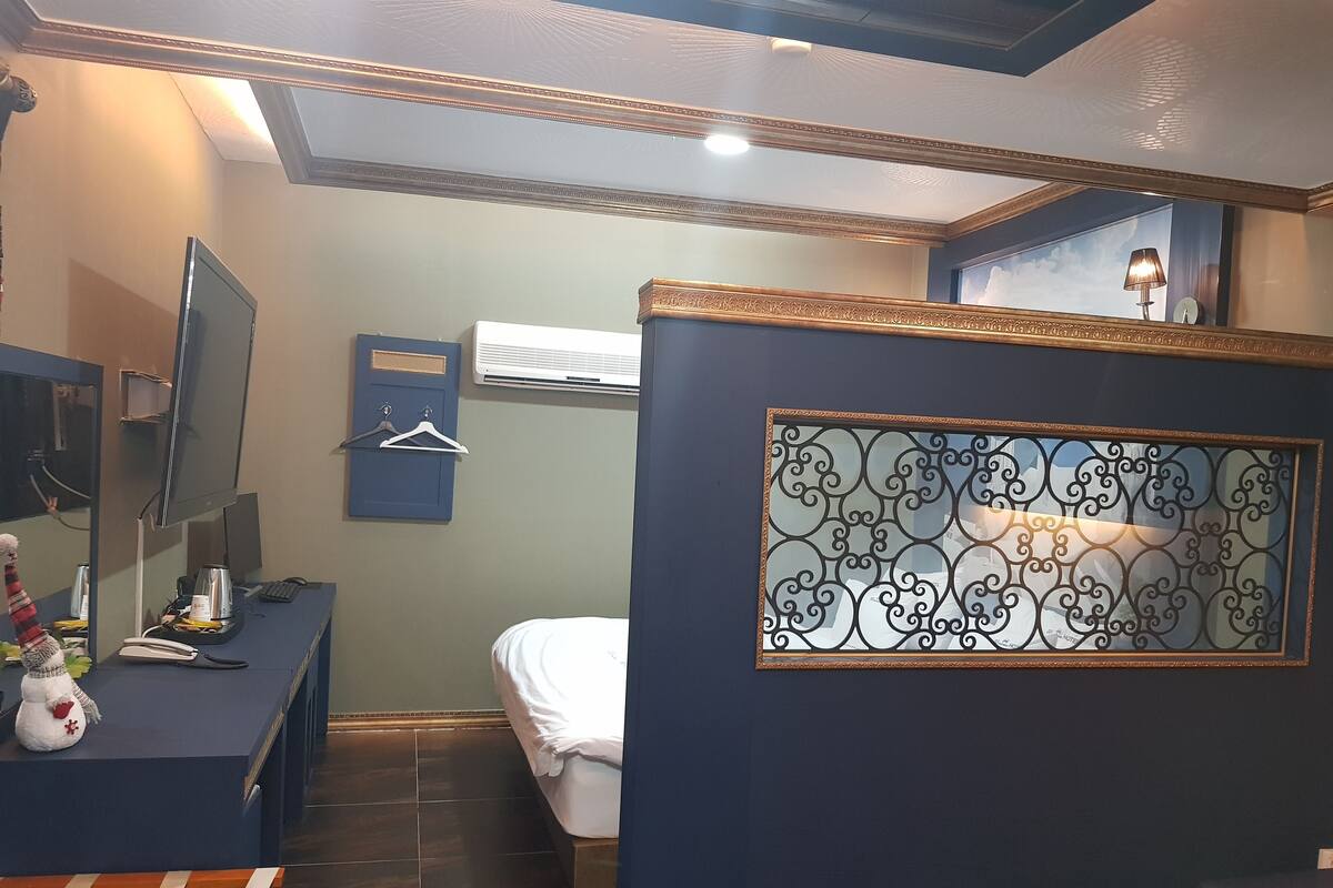 A hotel room with a bed, a desk with a computer, a chair, and a decorative wall panel.