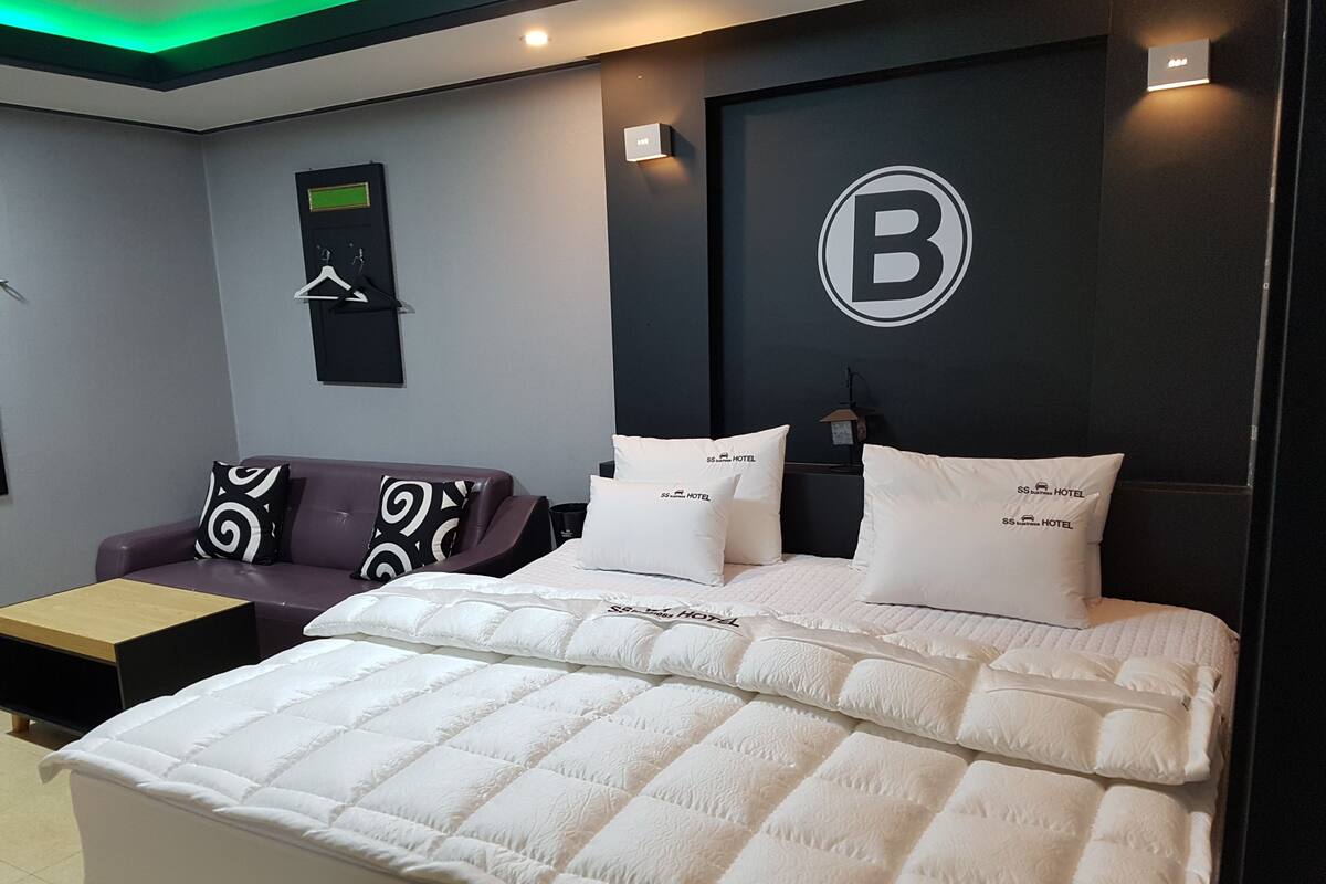 A modern hotel room with a large bed, a sofa, and a wall-mounted TV.