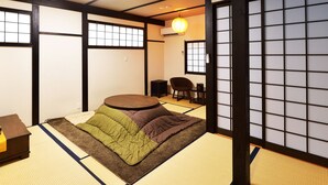 A tatami mat room with a futon bed, a round table, and a traditional Japanese sliding door. - karaku Inn (Kyoto)