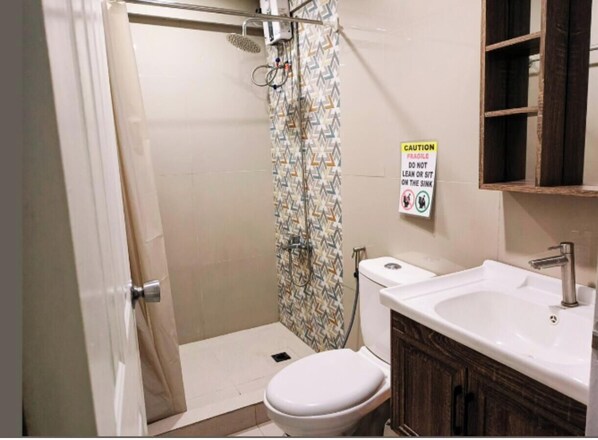 Un baño con ducha, inodoro, lavamanos y señal de precaución.