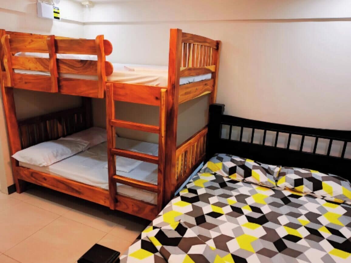 A bunk bed with a ladder, a single bed with a patterned bedspread, and a white wall with a small window.