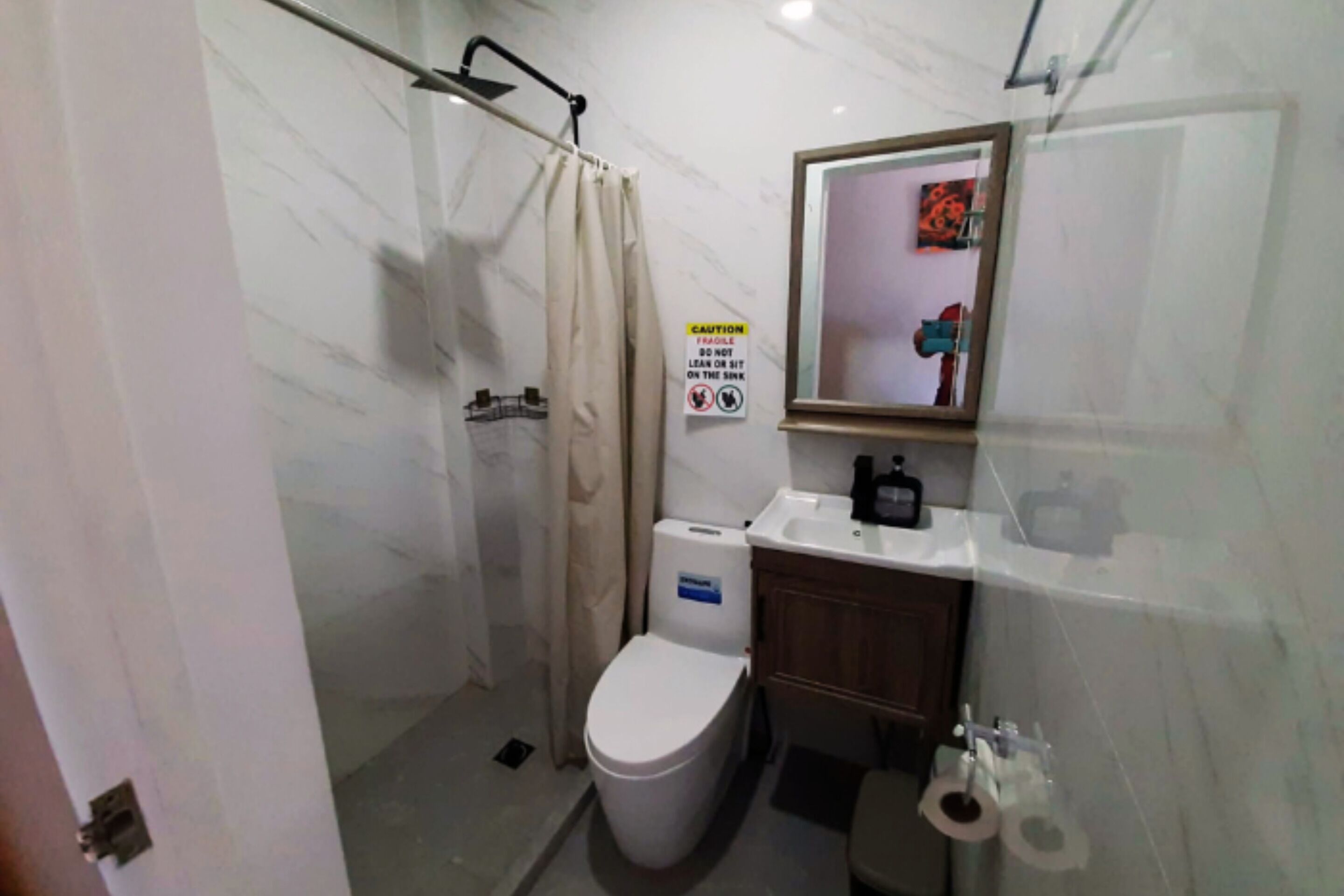 Een badkamer met toilet, wastafel, douche en een waarschuwingsbord.