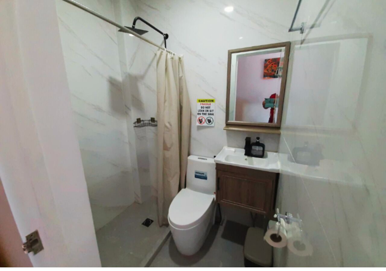 Een badkamer met toilet, wastafel en douche. Er hangt een waarschuwingsbord aan de muur.