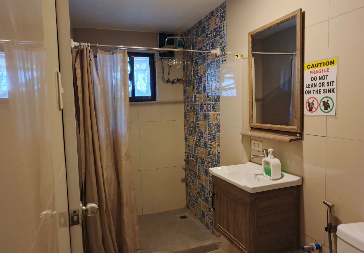 A bathroom with a shower, a sink, a caution sign, and a window.