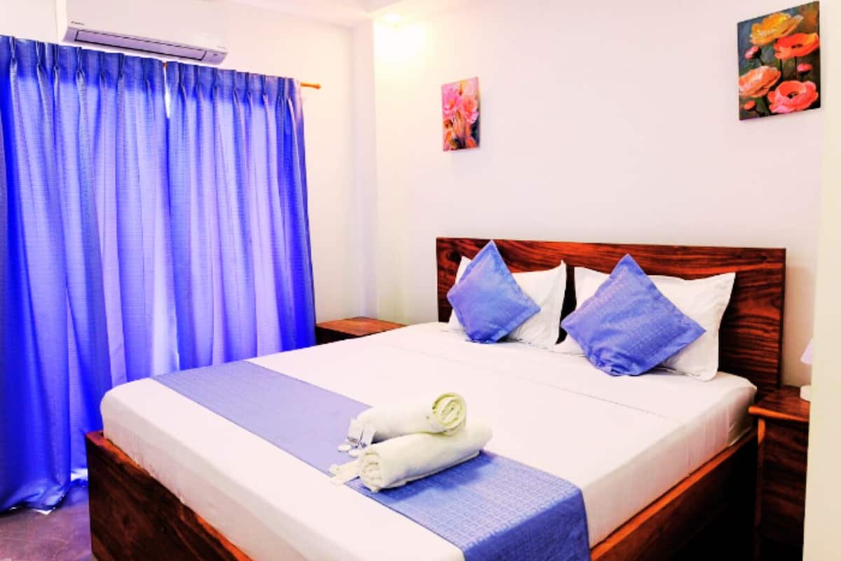 Una cama bien hecha con ropa de cama azul y blanca, cabecera de madera y cortina azul.