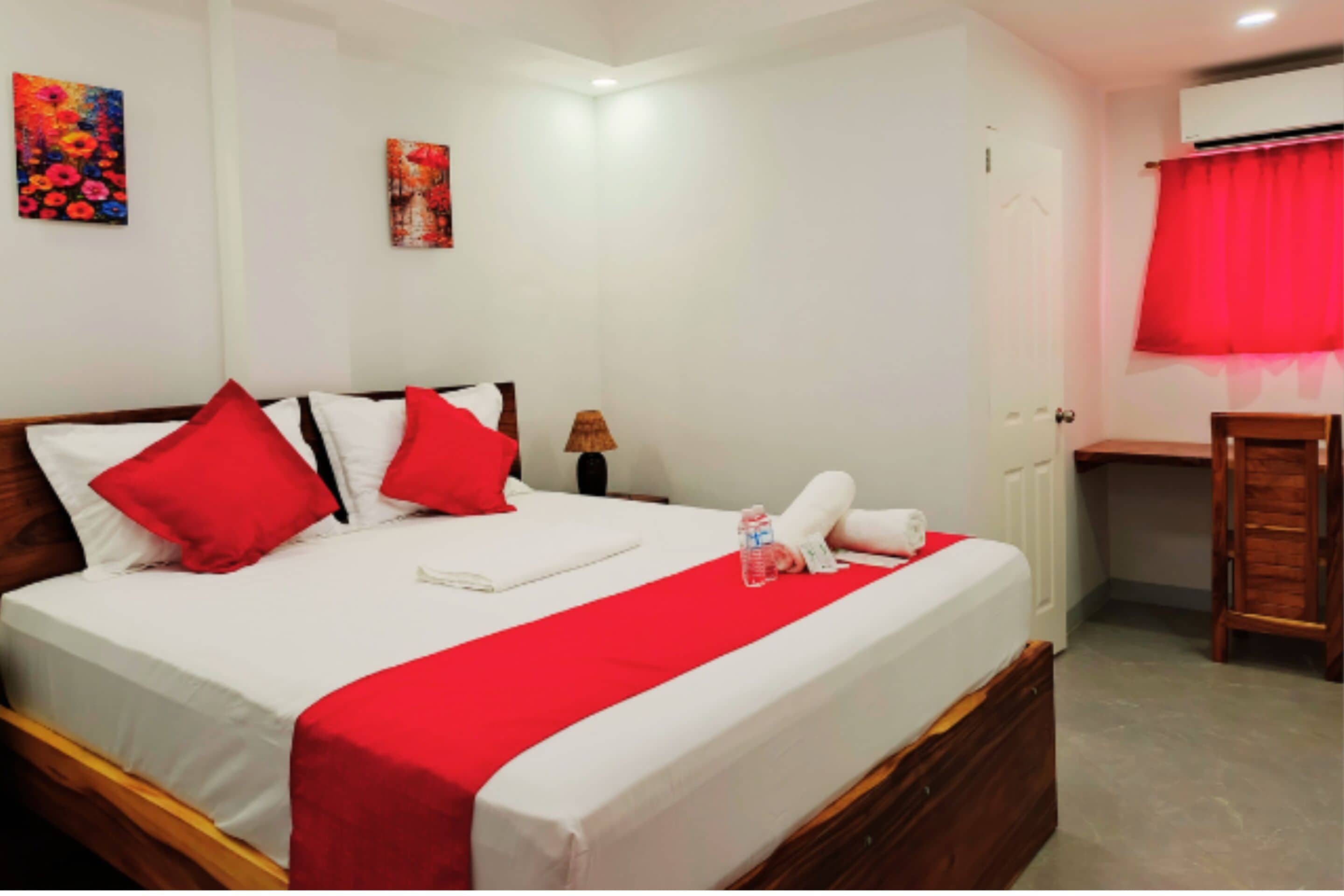 Una cama con ropa de cama roja, una mesita de noche, una lámpara y una cortina roja.