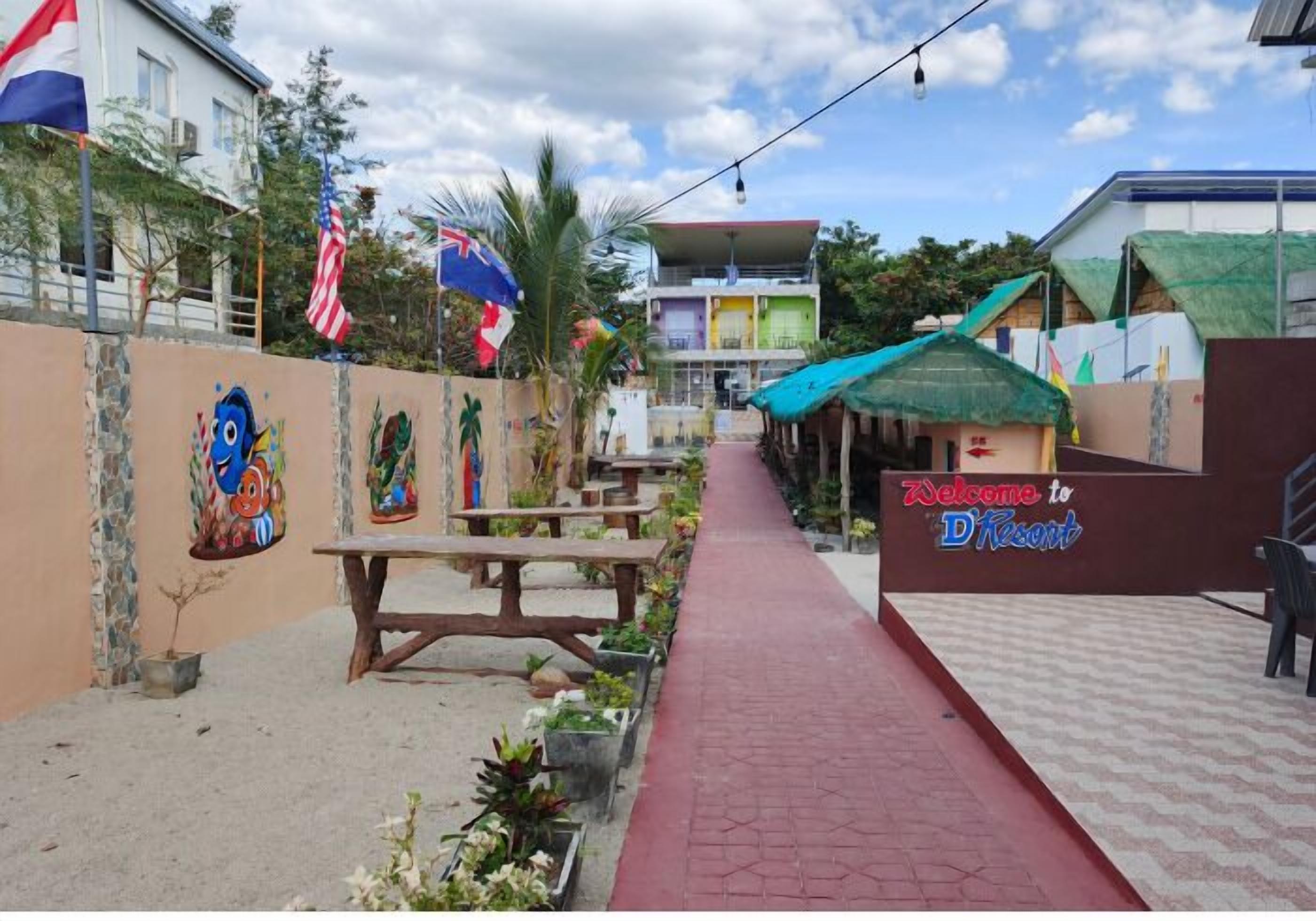 A pathway leading to a building with a 'Welcome to D' sign, surrounded by flags and outdoor seating.