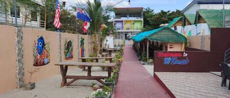 A pathway leading to a building with a 'Welcome to D' sign, surrounded by flags and outdoor seating.