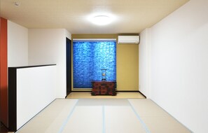A room with tatami flooring, a small wooden cabinet, and a window with blue blinds.