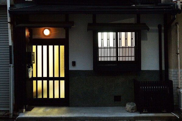 Une entrée de style japonais traditionnel, avec une porte coulissante et une fenêtre ornée de barreaux verticaux.