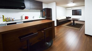 A modern kitchen with wooden bar stools, a built-in refrigerator, and a dining area with a table and sofa. - Raku Inn (Kyoto)
