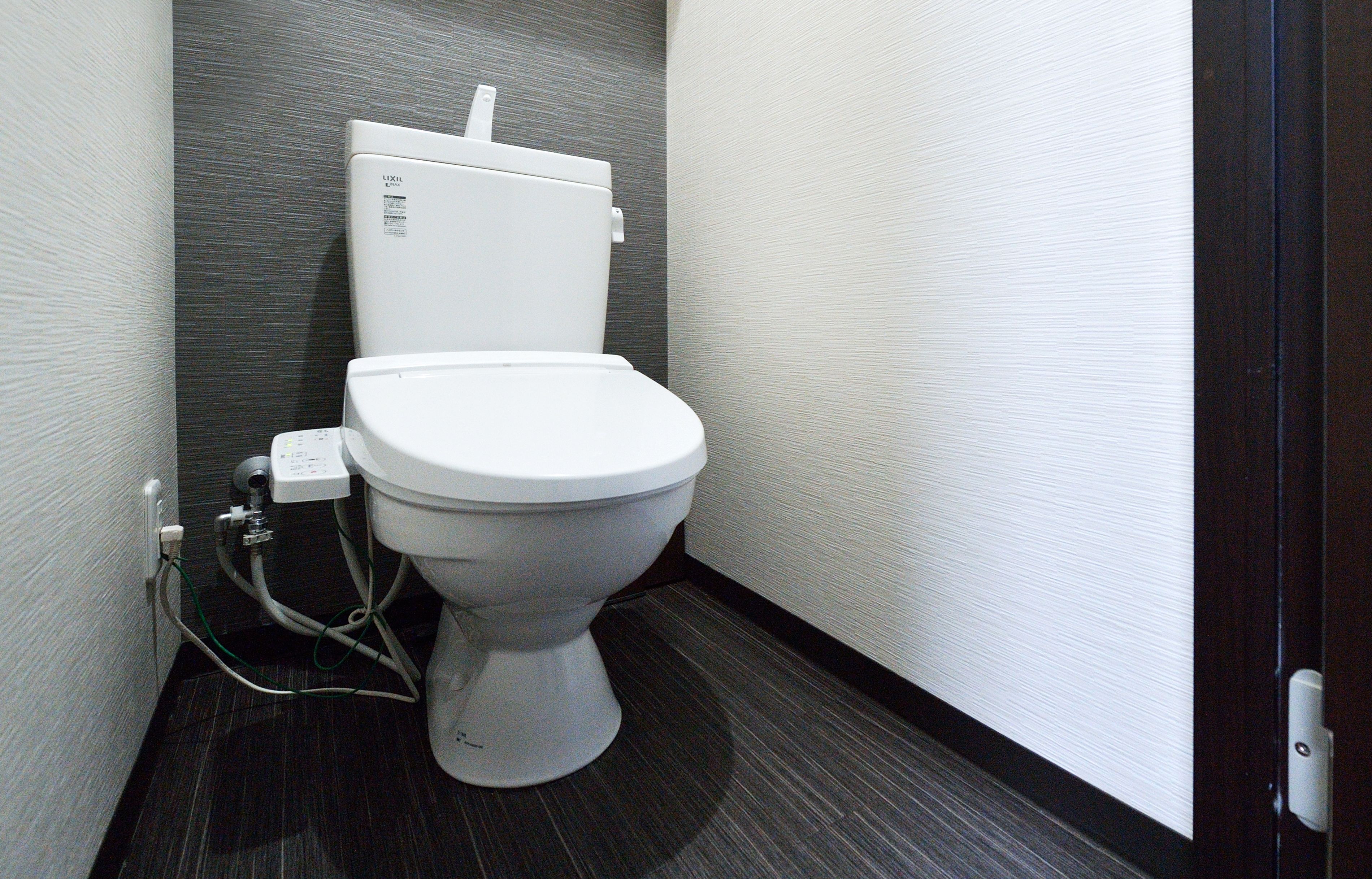 A modern bathroom with a white toilet, dark floor, and textured walls.