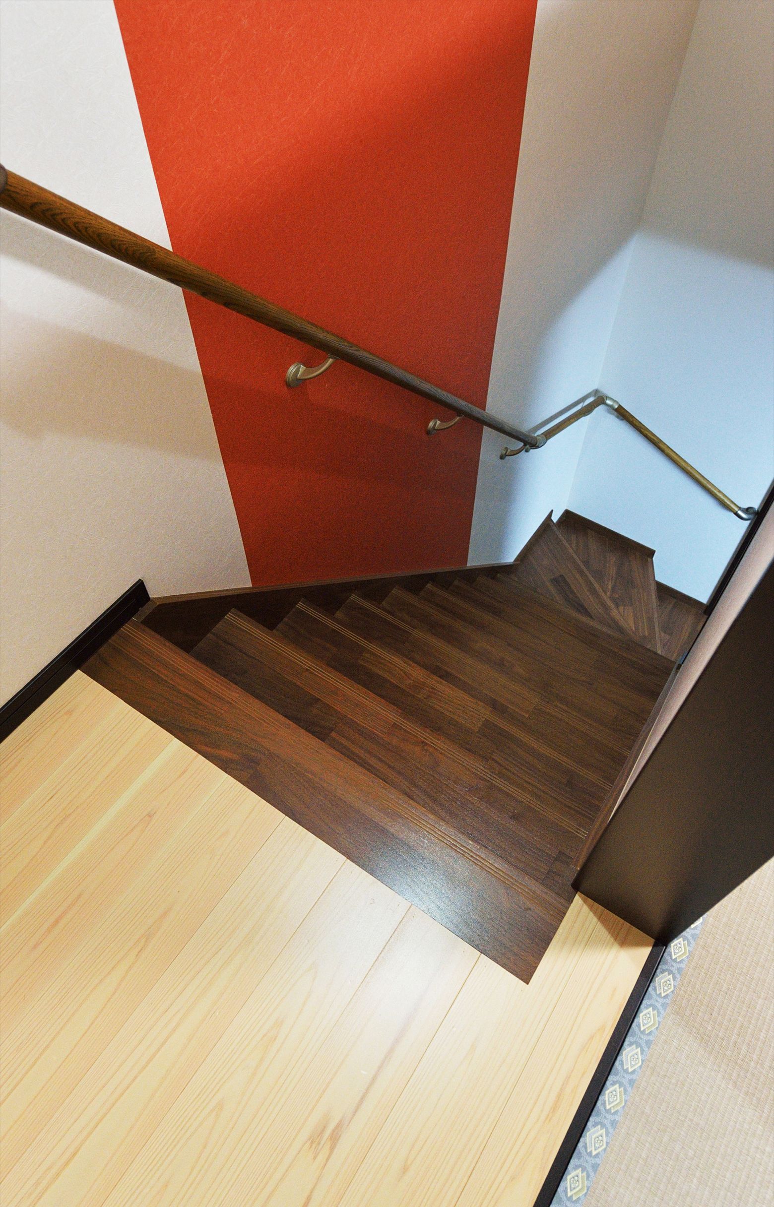 Un escalier en bois avec une rampe, menant à une pièce dont un mur est peint en rouge et l’autre en bleu clair.