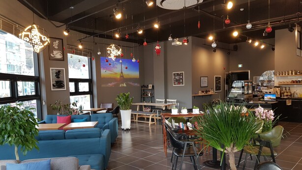Een modern café met een blauwe bank, eettafels en een koffiebar.