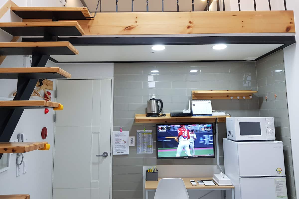 Cocina compacta con microondas, hervidor y televisión mostrando un partido de deportes.
